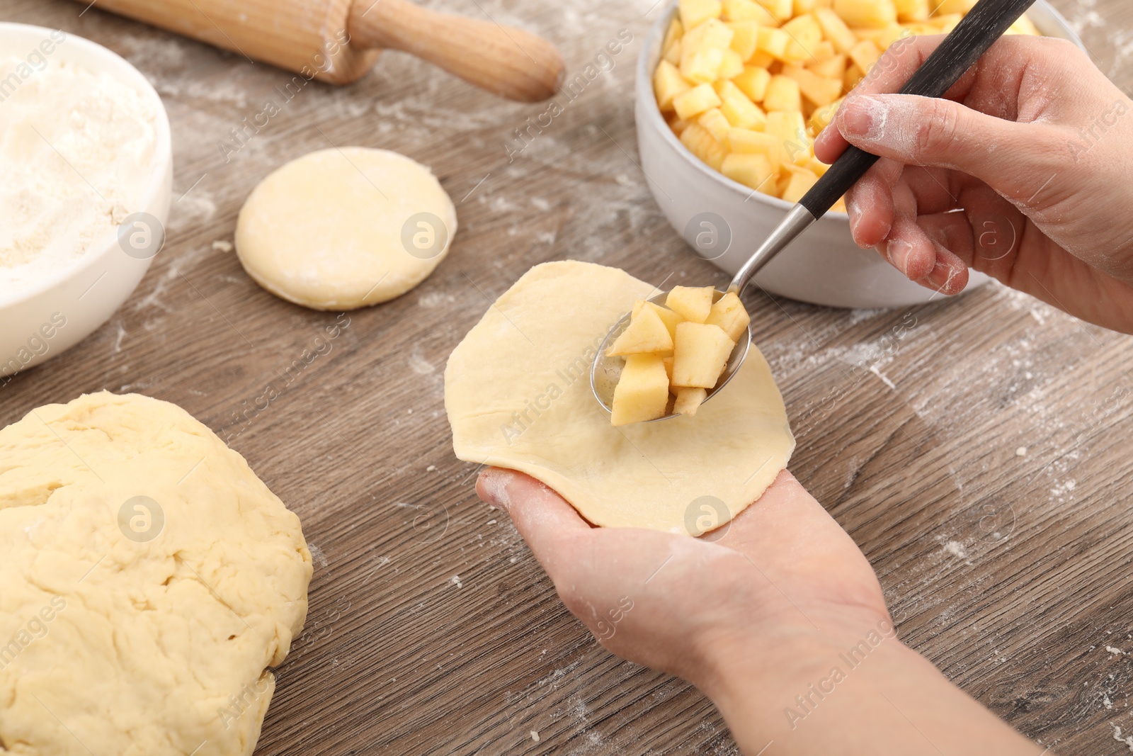 Photo of Woman making pirozhki (stuffed pastry pies) with apples at wooden table, closeup