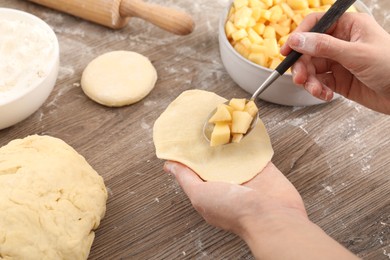 Photo of Woman making pirozhki (stuffed pastry pies) with apples at wooden table, closeup