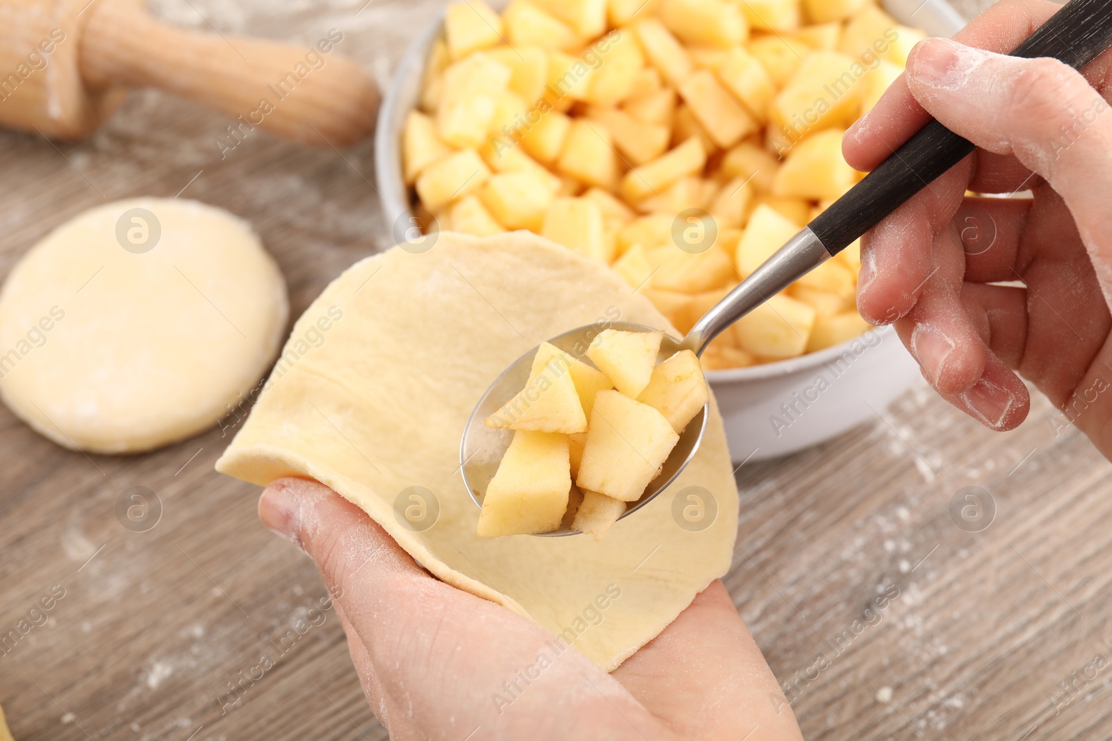 Photo of Woman making pirozhki (stuffed pastry pies) with apples at wooden table, closeup