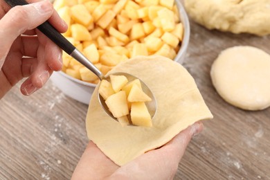 Photo of Woman making pirozhki (stuffed pastry pies) with apples at wooden table, closeup