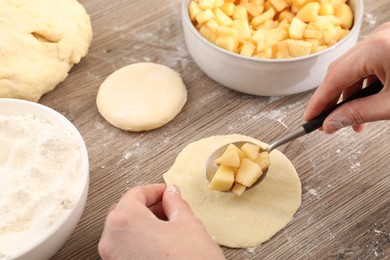 Photo of Woman making pirozhki (stuffed pastry pies) with apples at wooden table, closeup