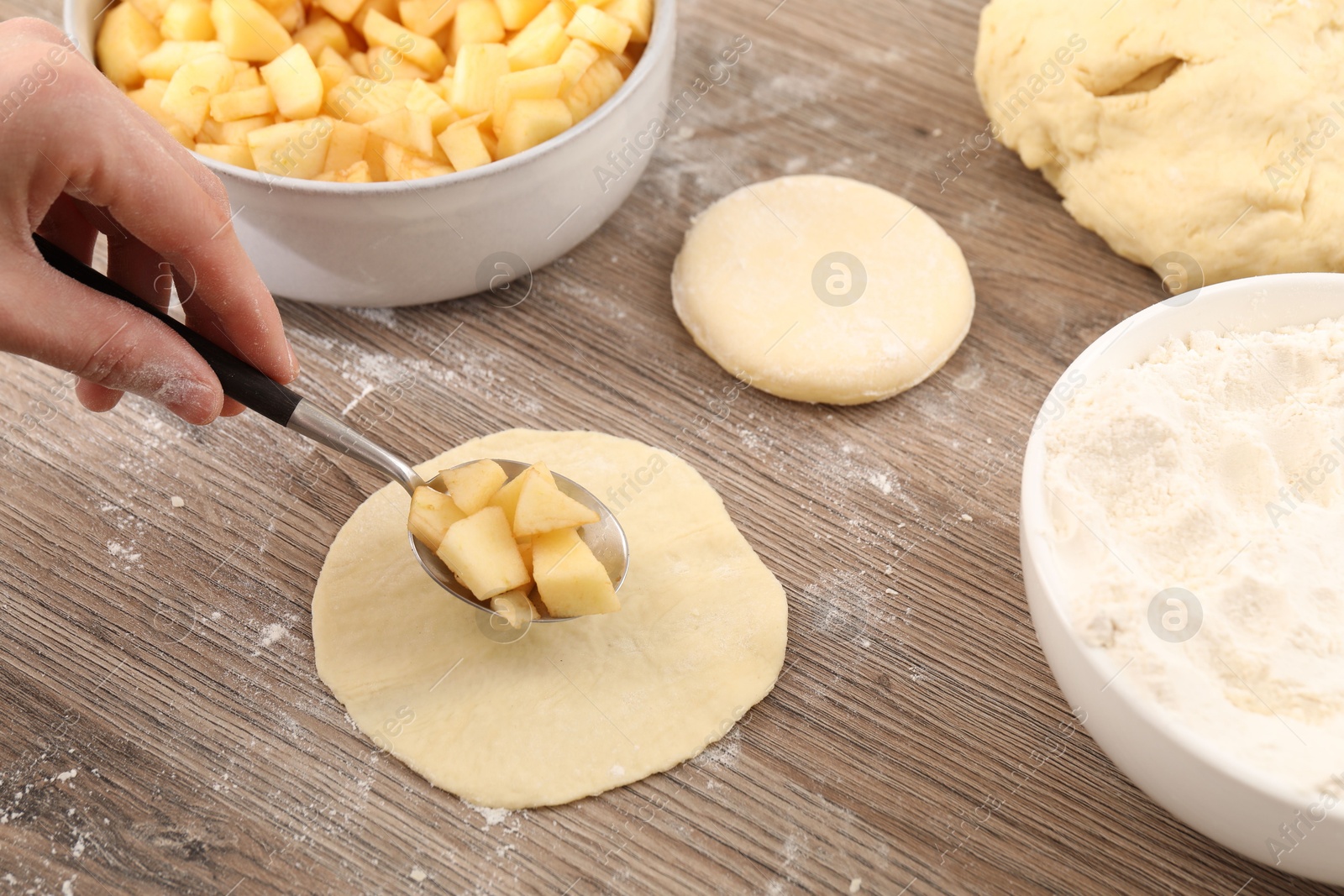 Photo of Woman making pirozhki (stuffed pastry pies) with apples at wooden table, closeup