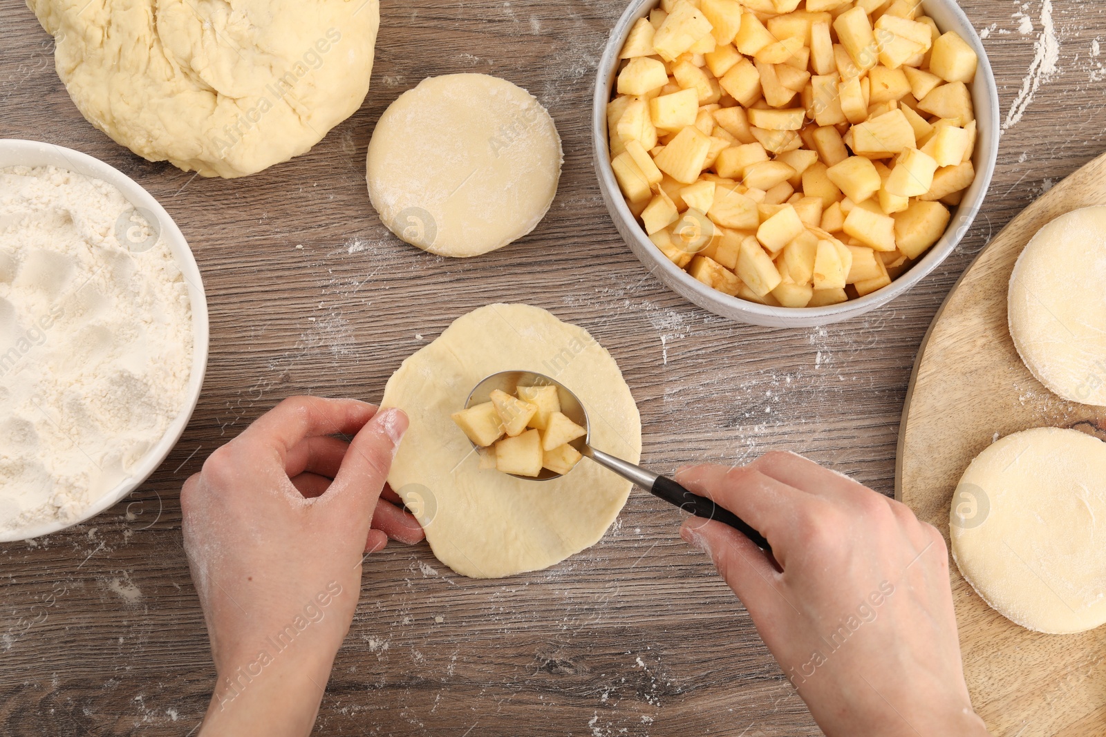 Photo of Woman making pirozhki (stuffed pastry pies) with apples at wooden table, top view