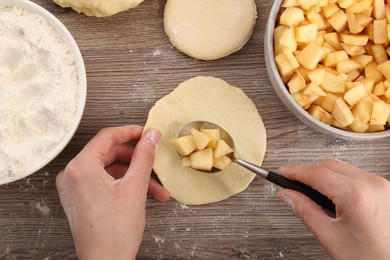 Photo of Woman making pirozhki (stuffed pastry pies) with apples at wooden table, top view