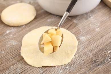 Photo of Making pirozhki (stuffed pastry pies). Putting apples onto piece of dough at wooden table, closeup