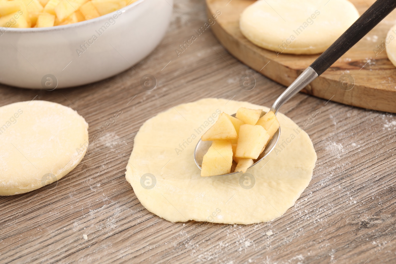 Photo of Making pirozhki (stuffed pastry pies). Putting apples onto piece of dough at wooden table, closeup