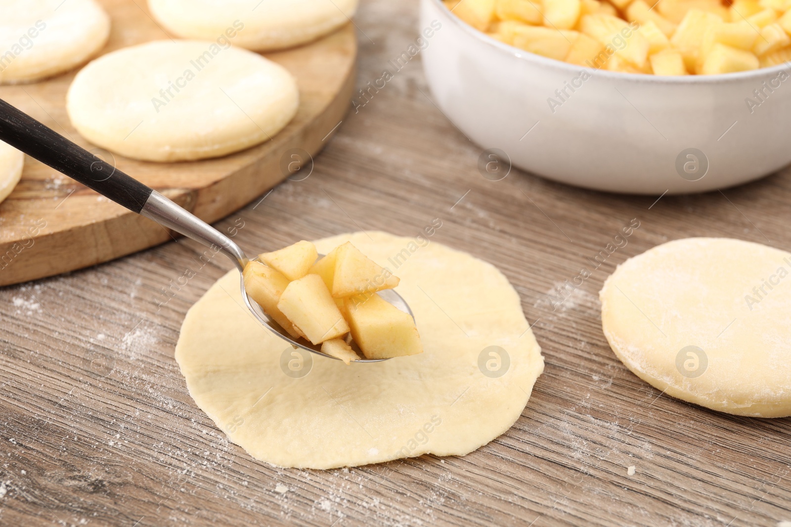 Photo of Making pirozhki (stuffed pastry pies). Putting apples onto piece of dough at wooden table, closeup