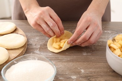 Photo of Woman making pirozhki (stuffed pastry pies) with apples at wooden table, closeup