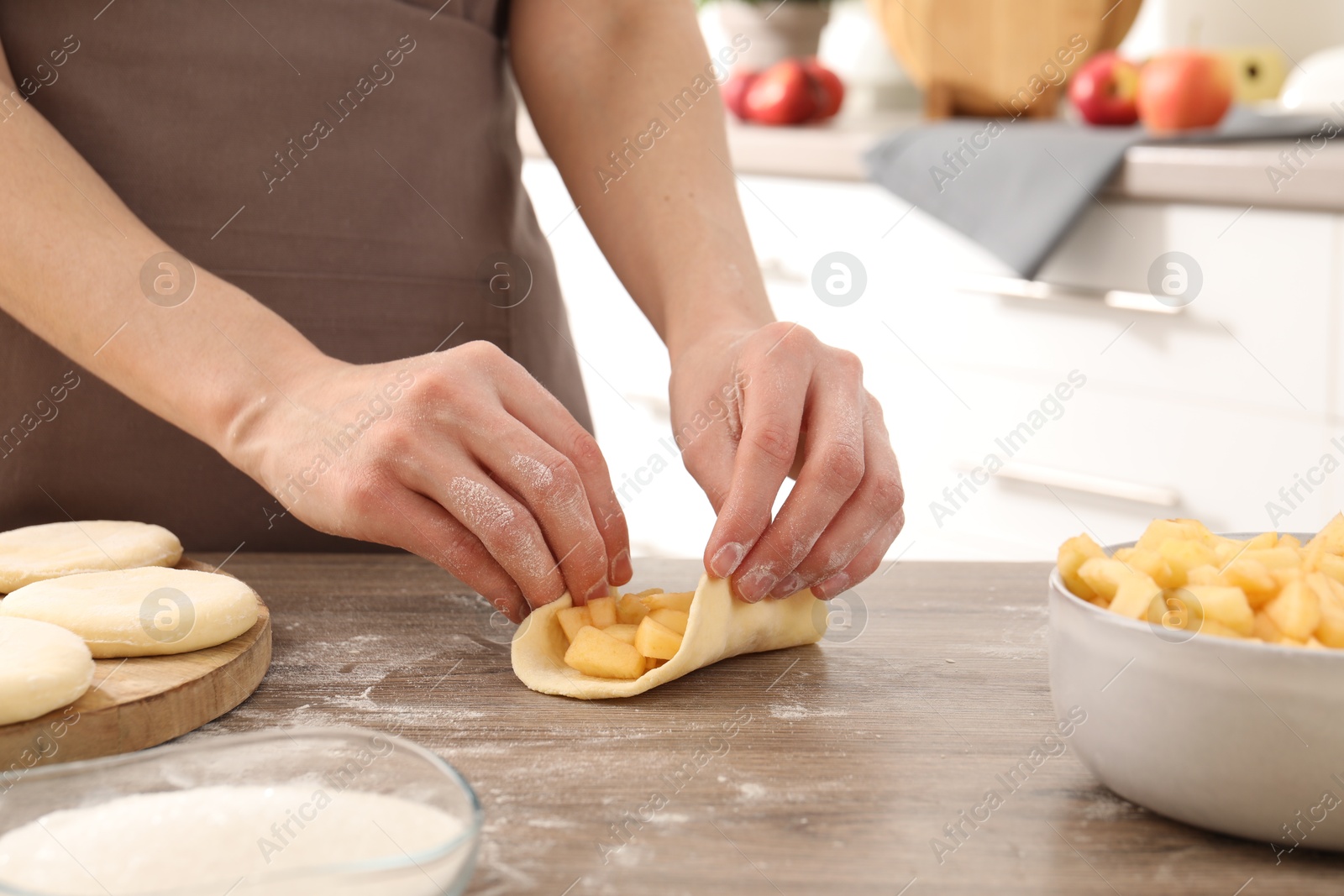 Photo of Woman making pirozhki (stuffed pastry pies) at wooden table indoors, closeup