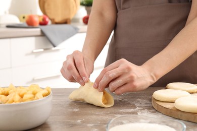 Photo of Woman making pirozhki (stuffed pastry pies) at wooden table indoors, closeup