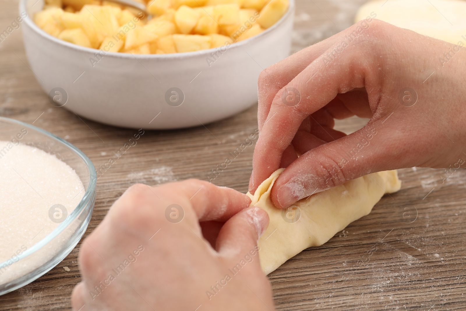 Photo of Woman making pirozhki (stuffed pastry pies) with apples at wooden table, closeup