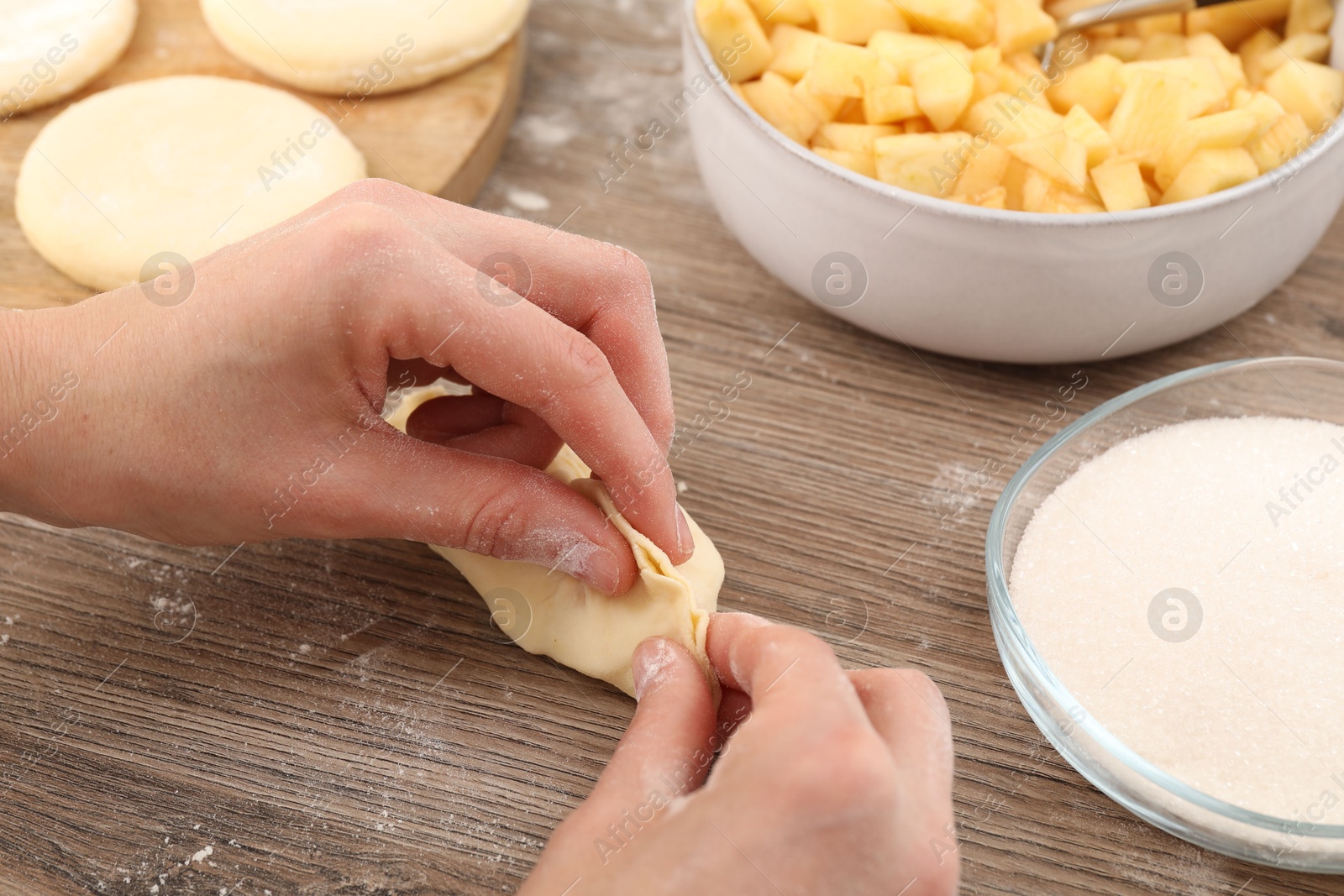 Photo of Woman making pirozhki (stuffed pastry pies) with apples at wooden table, closeup