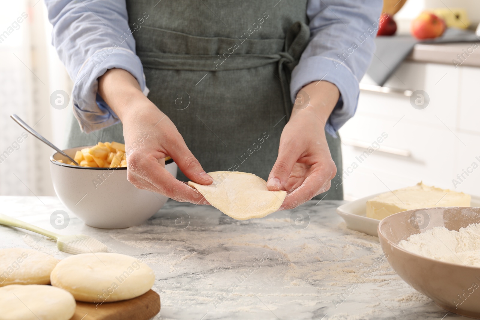 Photo of Woman making pirozhki (stuffed pastry pies) at white marble table indoors, closeup