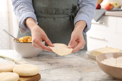 Photo of Woman making pirozhki (stuffed pastry pies) at white marble table indoors, closeup