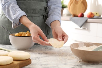 Photo of Woman making pirozhki (stuffed pastry pies) at white marble table indoors, closeup