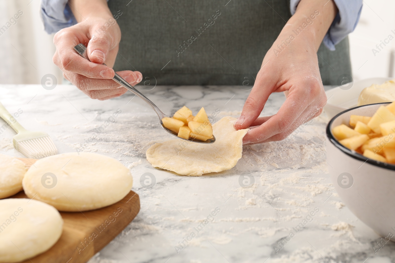 Photo of Woman making pirozhki (stuffed pastry pies) with apples at white marble table, closeup