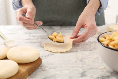 Photo of Woman making pirozhki (stuffed pastry pies) with apples at white marble table, closeup