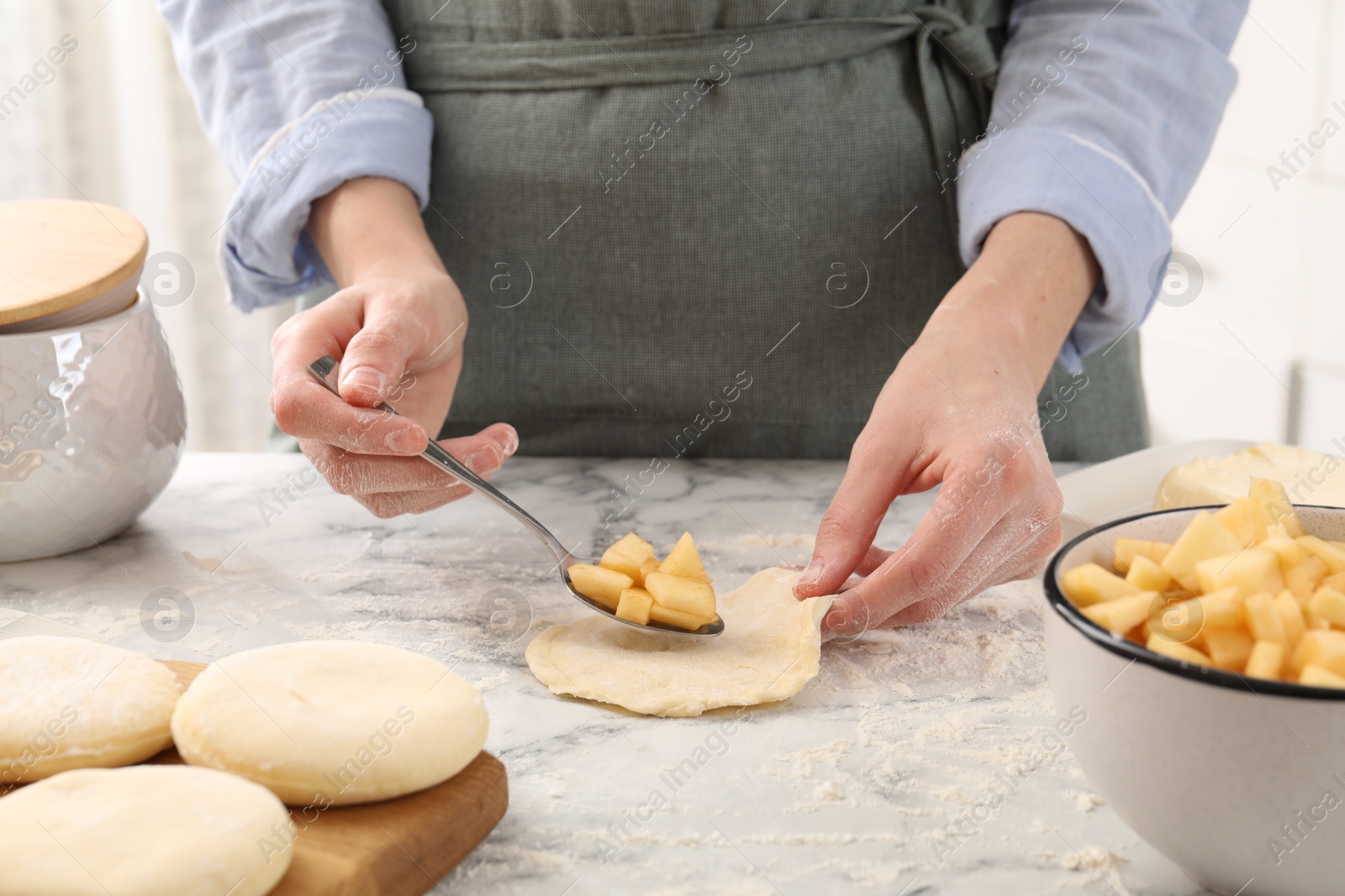 Photo of Woman making pirozhki (stuffed pastry pies) with apples at white marble table, closeup