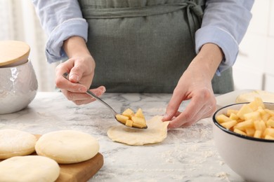 Photo of Woman making pirozhki (stuffed pastry pies) with apples at white marble table, closeup