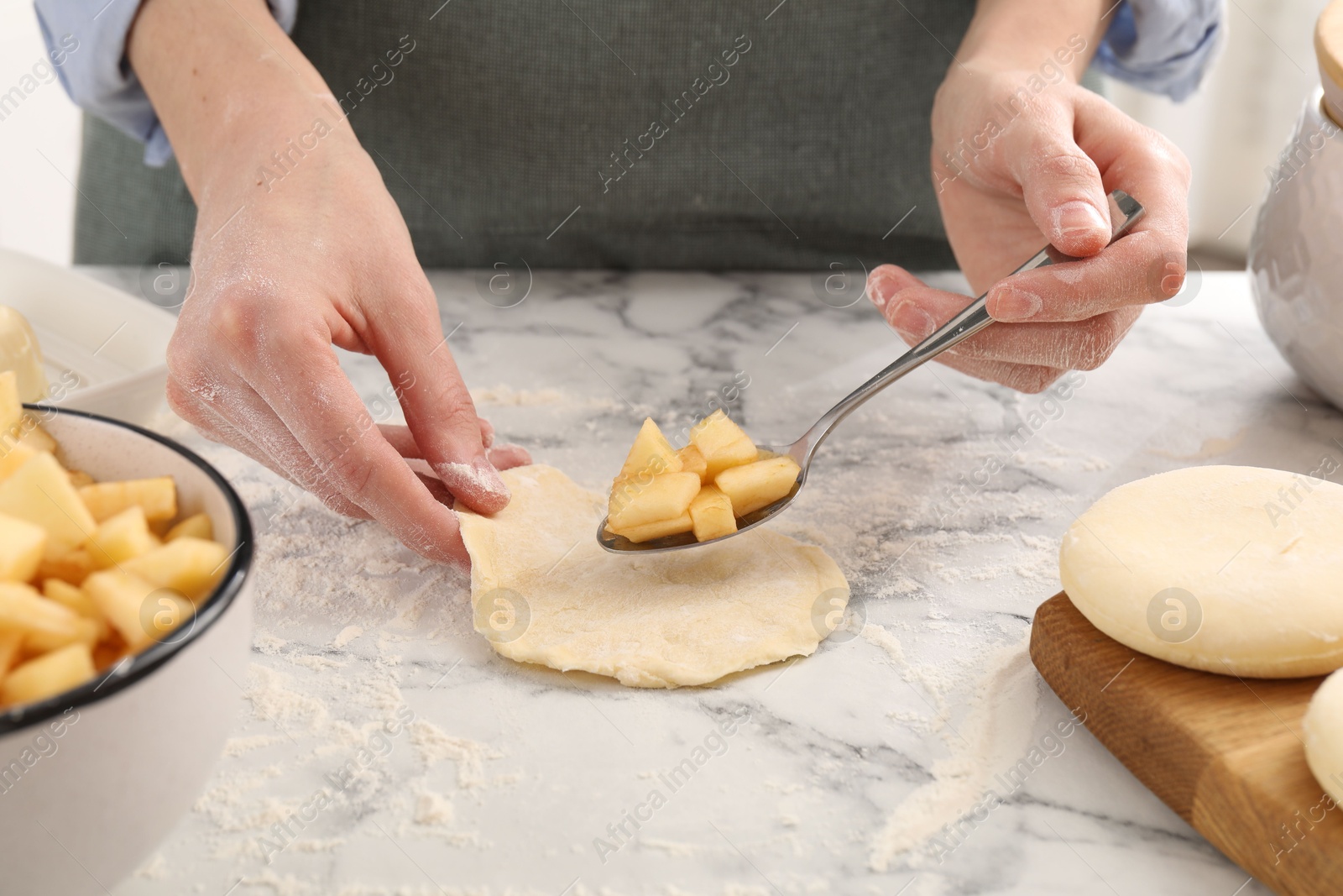 Photo of Woman making pirozhki (stuffed pastry pies) with apples at white marble table, closeup