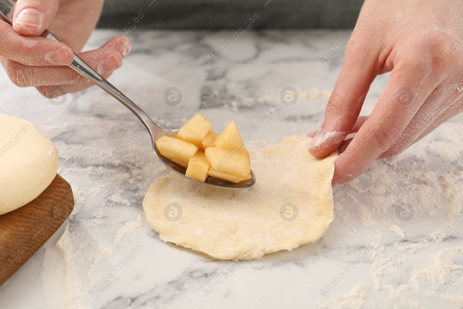 Photo of Woman making pirozhki (stuffed pastry pies) with apples at white marble table, closeup