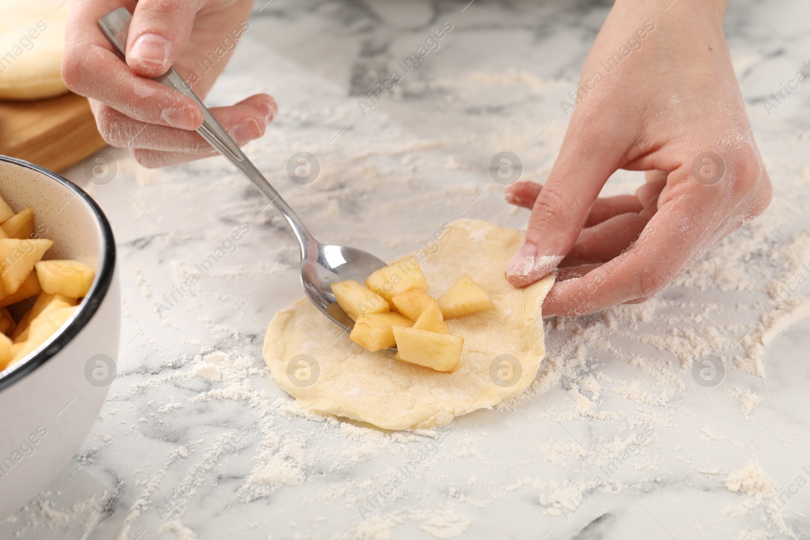 Photo of Woman making pirozhki (stuffed pastry pies) with apples at white marble table, closeup