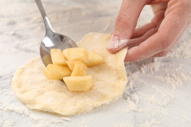 Photo of Woman making pirozhki (stuffed pastry pies) with apples at white marble table, closeup