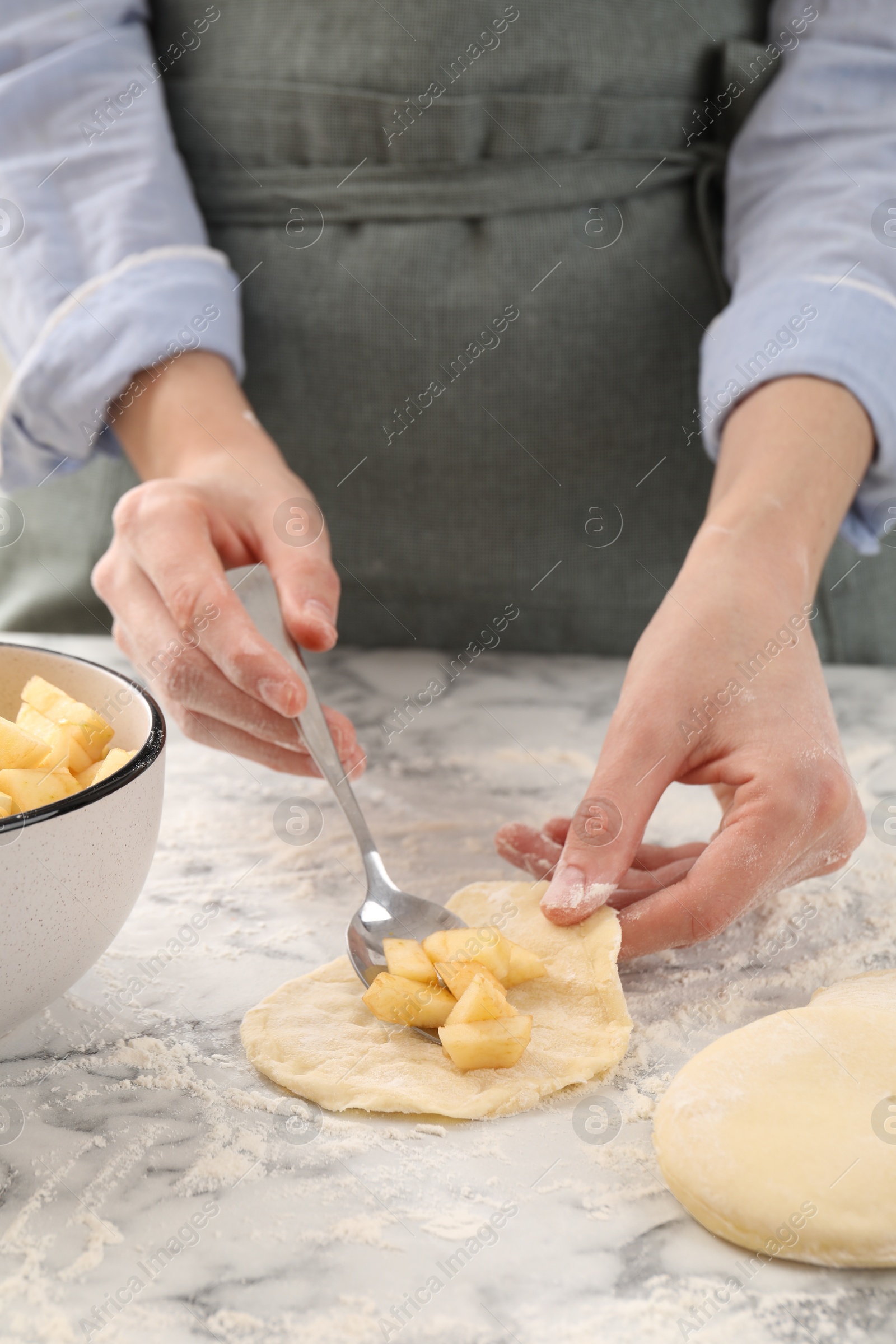 Photo of Woman making pirozhki (stuffed pastry pies) with apples at white marble table, closeup