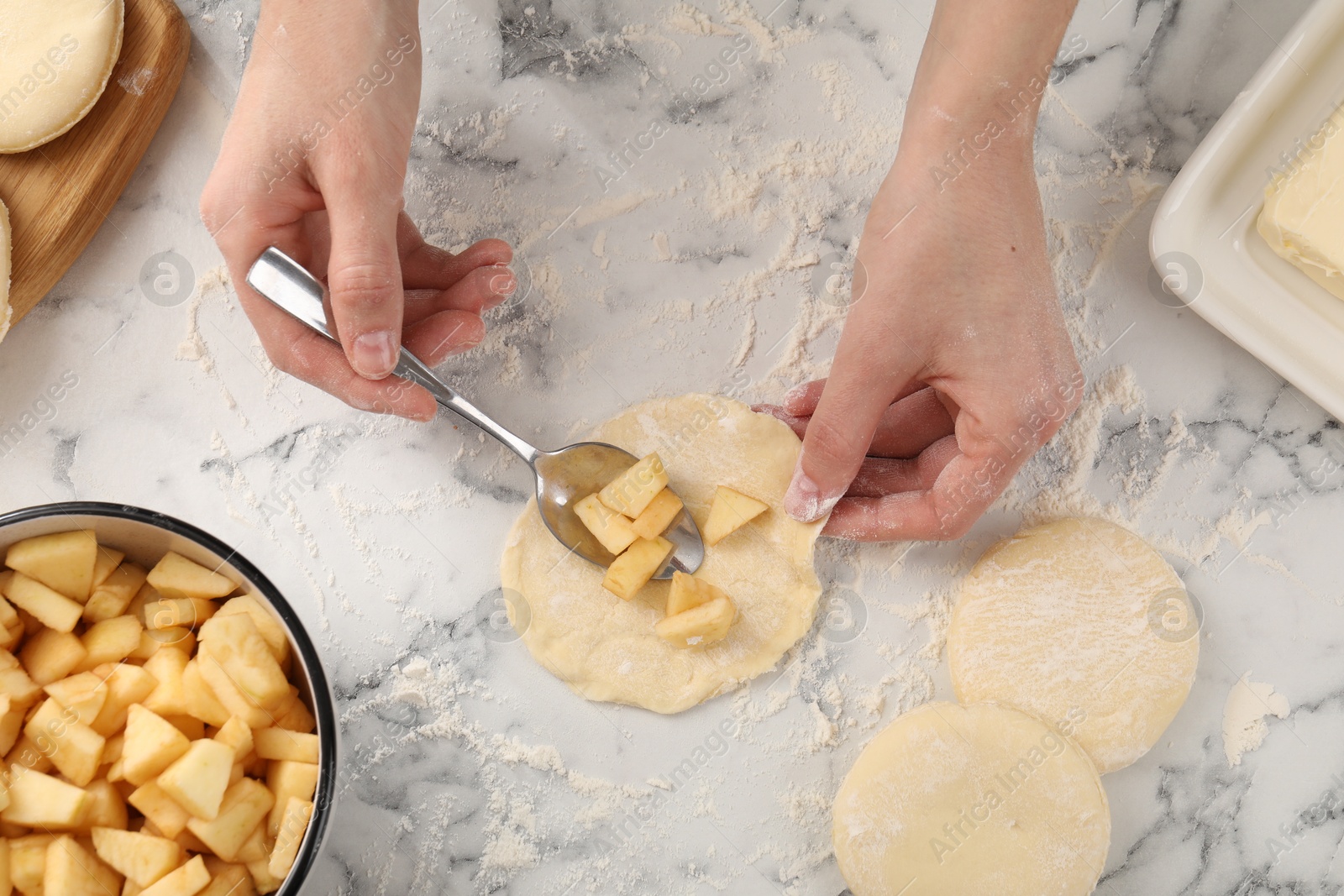 Photo of Woman making pirozhki (stuffed pastry pies) with apples at white marble table, top view