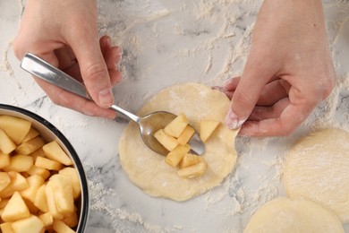 Photo of Woman making pirozhki (stuffed pastry pies) with apples at white marble table, top view