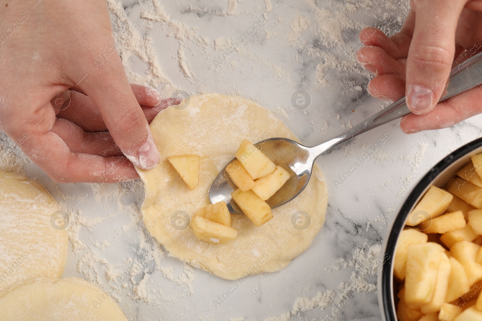 Photo of Woman making pirozhki (stuffed pastry pies) with apples at white marble table, top view