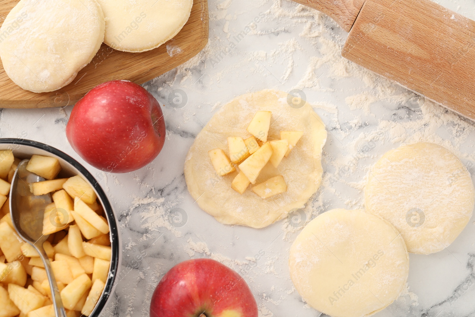 Photo of Making pirozhki (stuffed pastry pies). Pieces of dough with apples on white marble table, flat lay