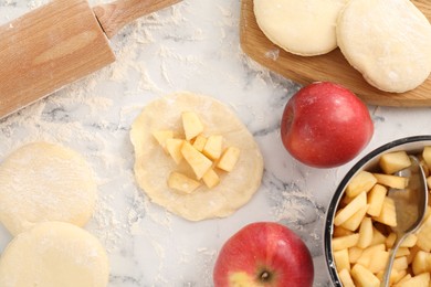 Photo of Making pirozhki (stuffed pastry pies). Pieces of dough with apples on white marble table, flat lay