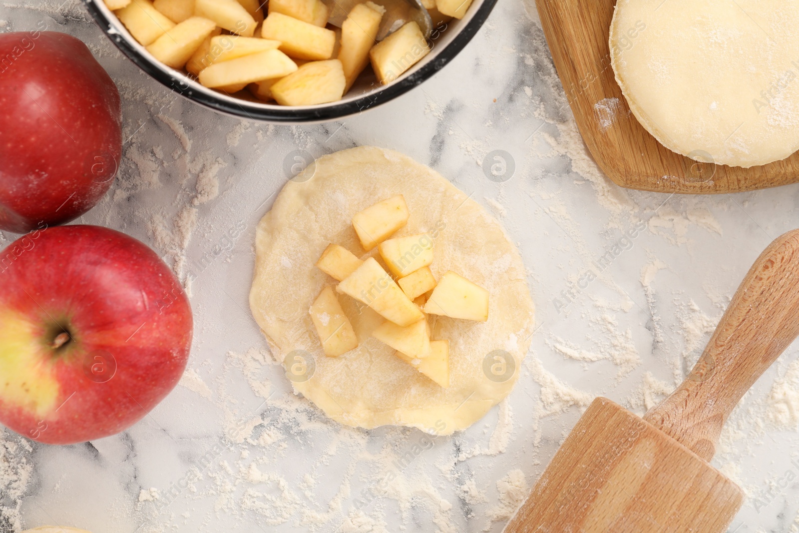 Photo of Making pirozhki (stuffed pastry pies). Pieces of dough with apples on white marble table, flat lay