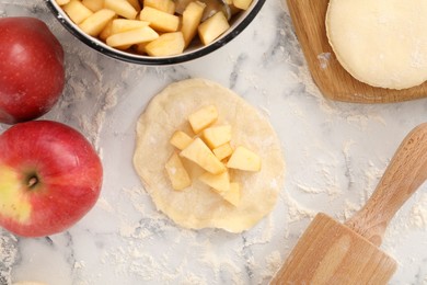 Photo of Making pirozhki (stuffed pastry pies). Pieces of dough with apples on white marble table, flat lay