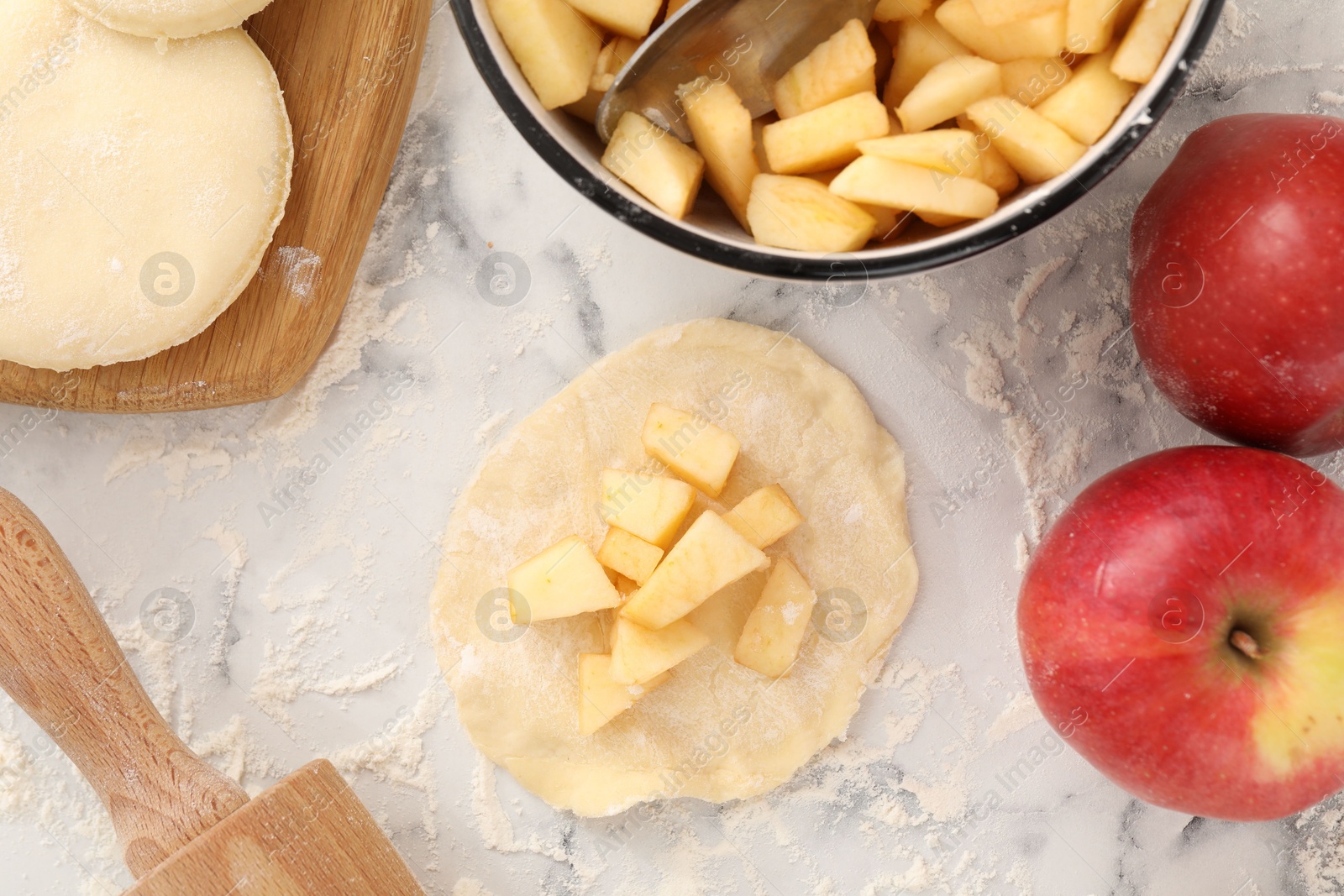 Photo of Making pirozhki (stuffed pastry pies). Pieces of dough with apples on white marble table, flat lay