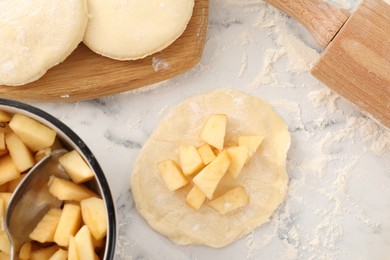 Photo of Making pirozhki (stuffed pastry pies). Pieces of dough with apples on white marble table, flat lay