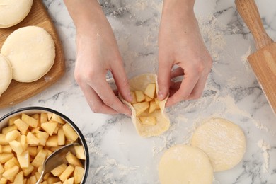 Photo of Woman making pirozhki (stuffed pastry pies) with apples at white marble table, top view