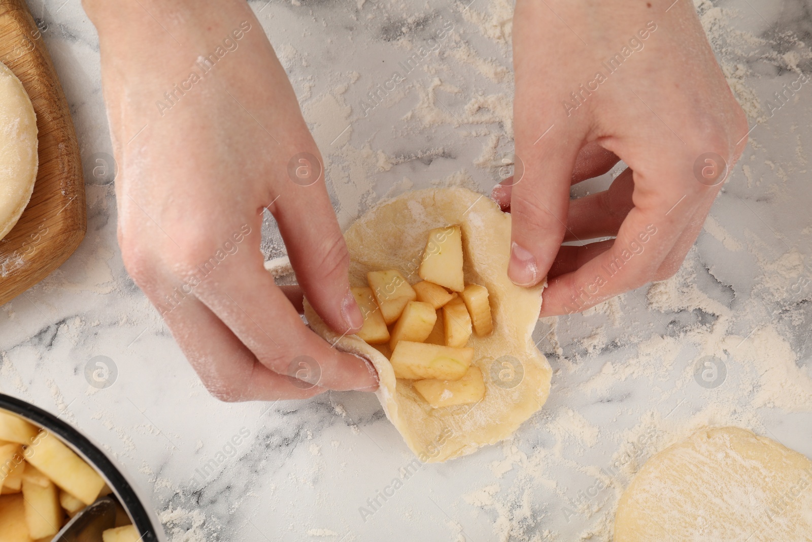 Photo of Woman making pirozhki (stuffed pastry pies) with apples at white marble table, top view