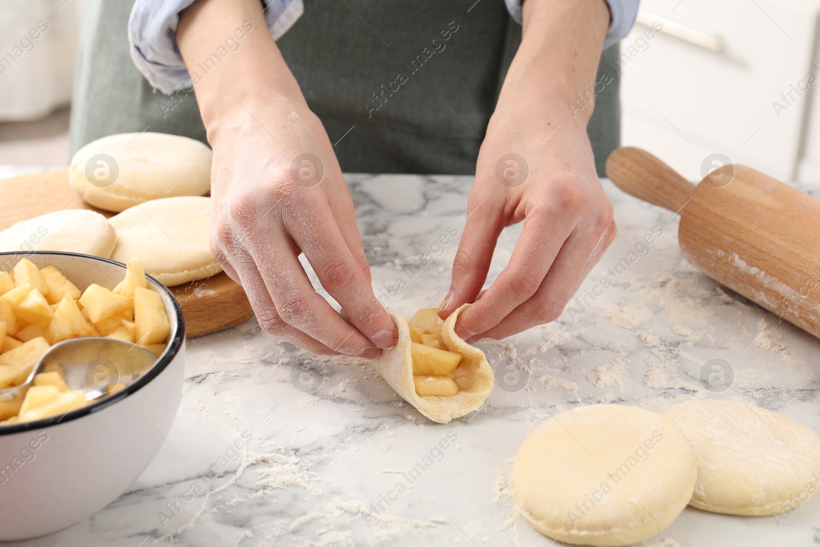 Photo of Woman making pirozhki (stuffed pastry pies) with apples at white marble table indoors, closeup