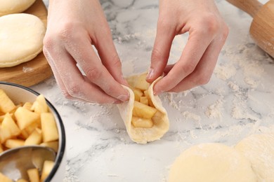 Photo of Woman making pirozhki (stuffed pastry pies) with apples at white marble table, closeup