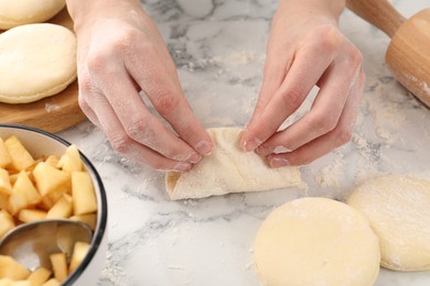 Photo of Woman making pirozhki (stuffed pastry pies) with apples at white marble table, closeup