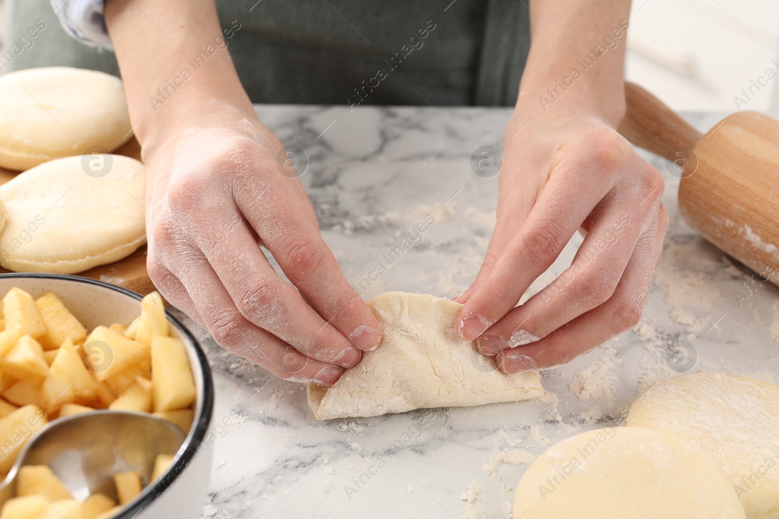 Photo of Woman making pirozhki (stuffed pastry pies) with apples at white marble table indoors, closeup