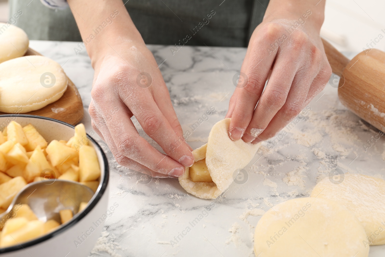 Photo of Woman making pirozhki (stuffed pastry pies) with apples at white marble table, closeup