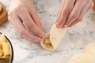 Photo of Woman making pirozhki (stuffed pastry pies) with apples at white marble table, closeup