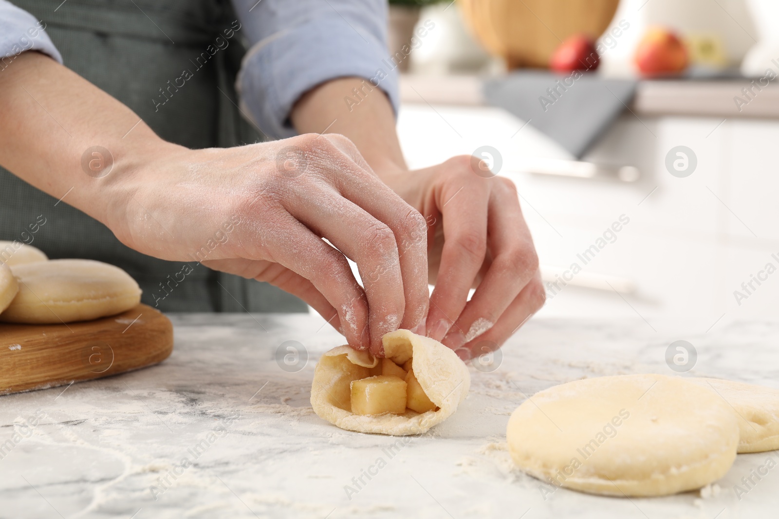 Photo of Woman making pirozhki (stuffed pastry pies) with apples at white marble table indoors, closeup