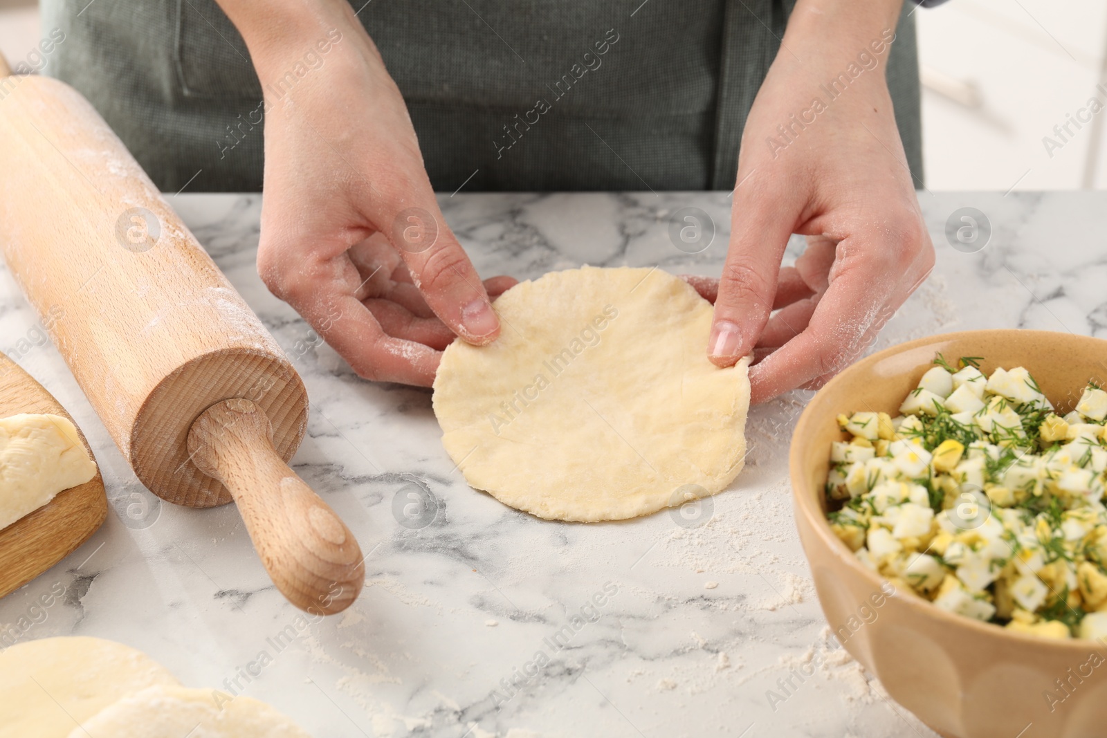 Photo of Woman making pirozhki (stuffed pastry pies) at white marble table indoors, closeup