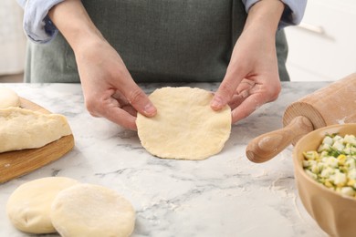 Photo of Woman making pirozhki (stuffed pastry pies) at white marble table indoors, closeup