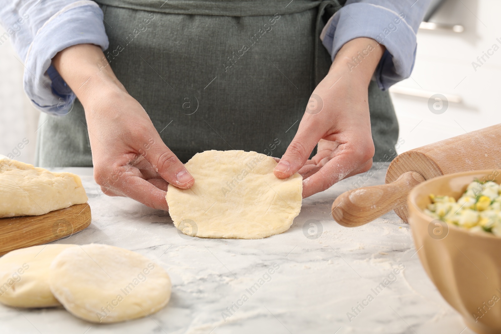 Photo of Woman making pirozhki (stuffed pastry pies) at white marble table indoors, closeup