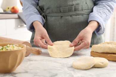 Photo of Woman making pirozhki (stuffed pastry pies) at white marble table indoors, closeup